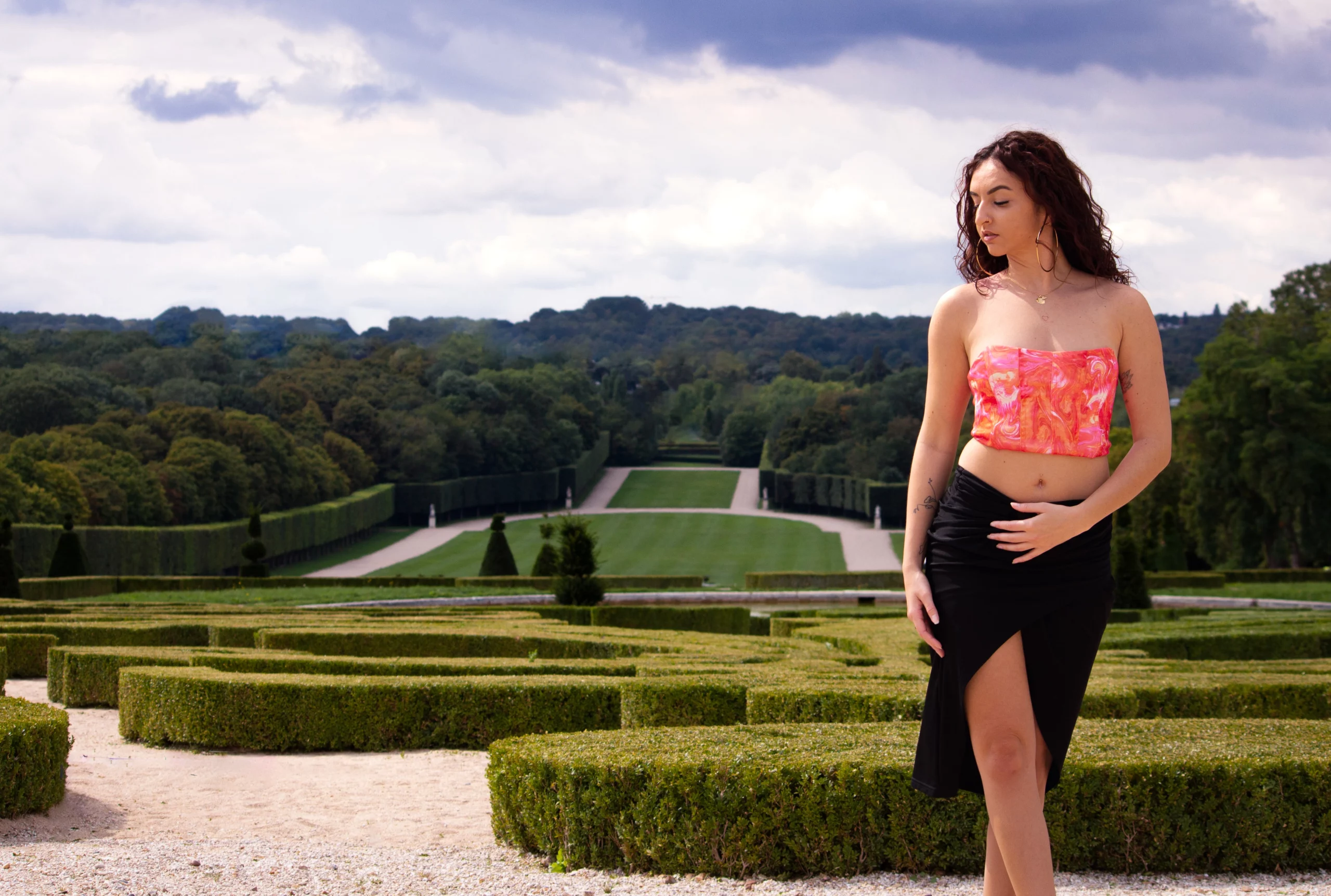 Jeune femme en haut coloré posant dans les jardins du château de Sceaux avec les grandes allées en arrière-plan