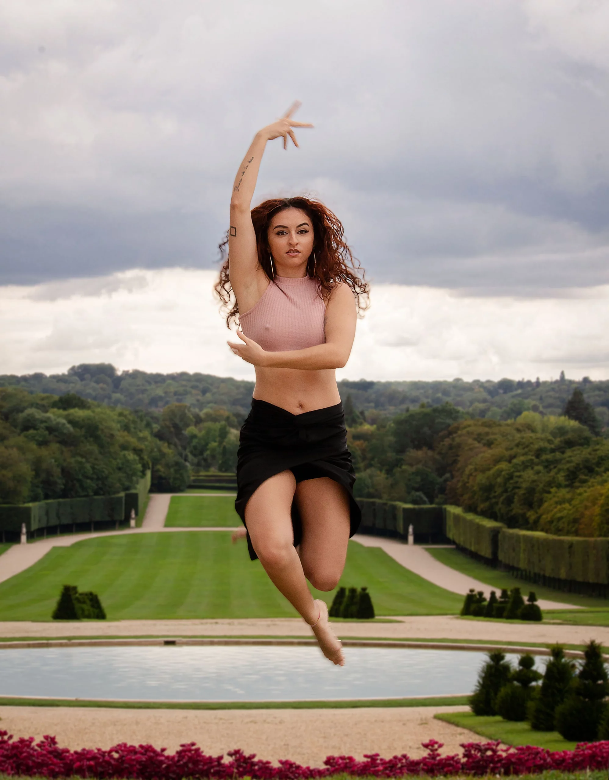 Femme en jupe noire effectuant un saut artistique dans les jardins du château de Sceaux devant les allées verdoyantes