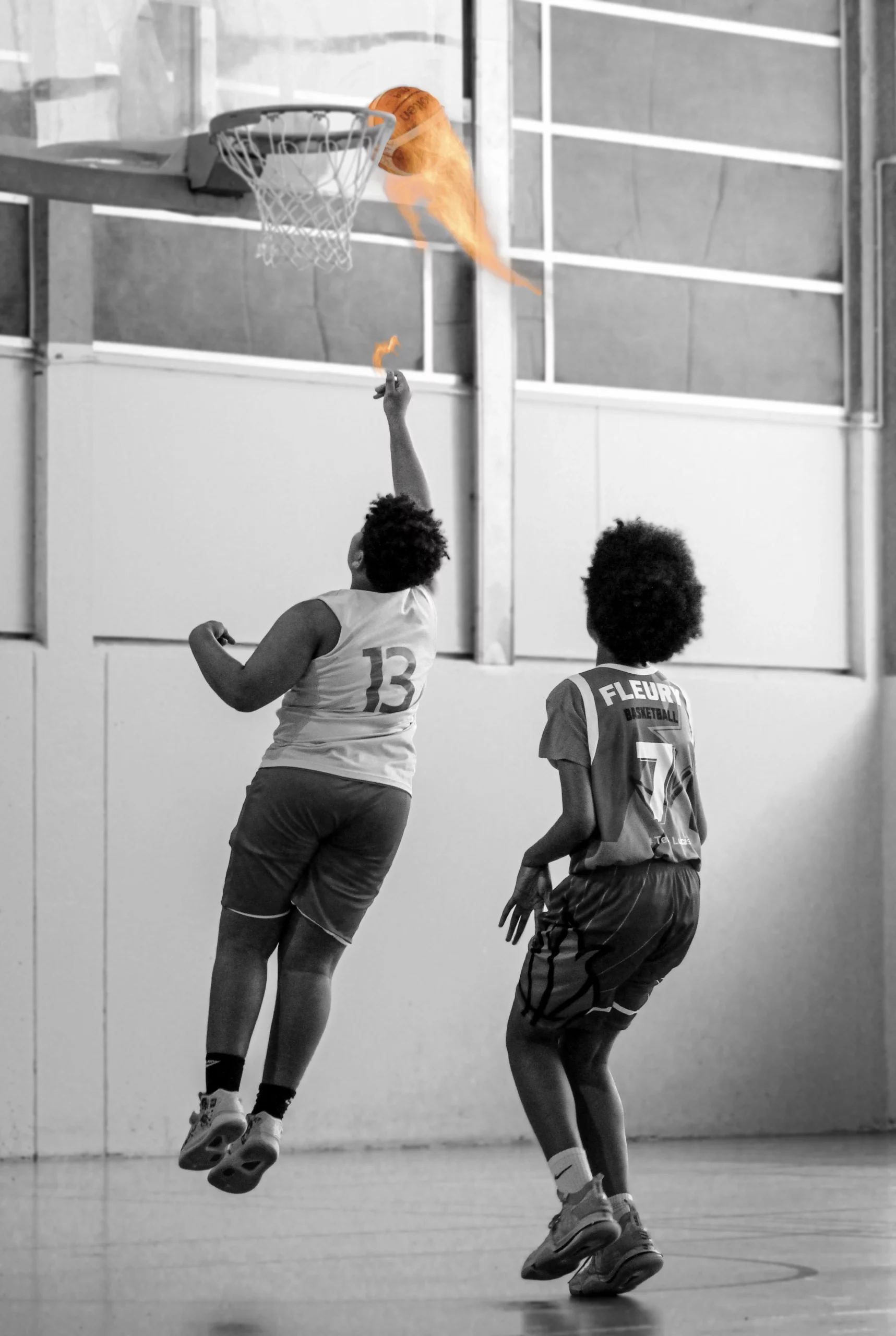 Photographie en noir et blanc d'un joueur de basket en plein saut avec sa balle enflammée.
