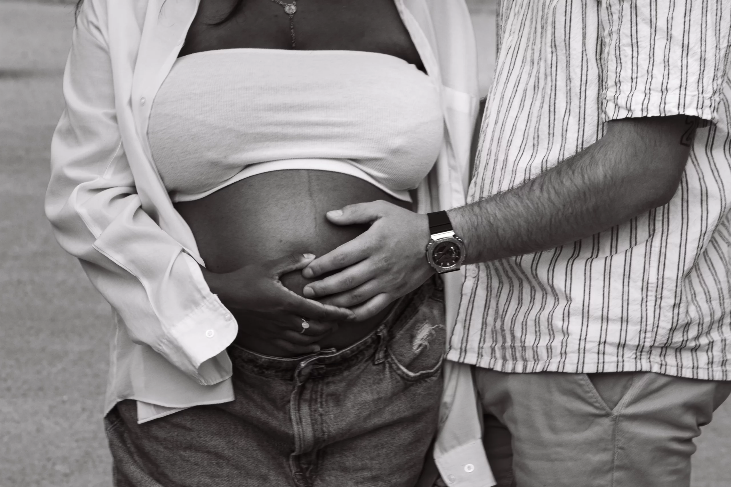 Photographie de détail d'un ventre d'une femme enceinte avec son mari qui lui tient le ventre.