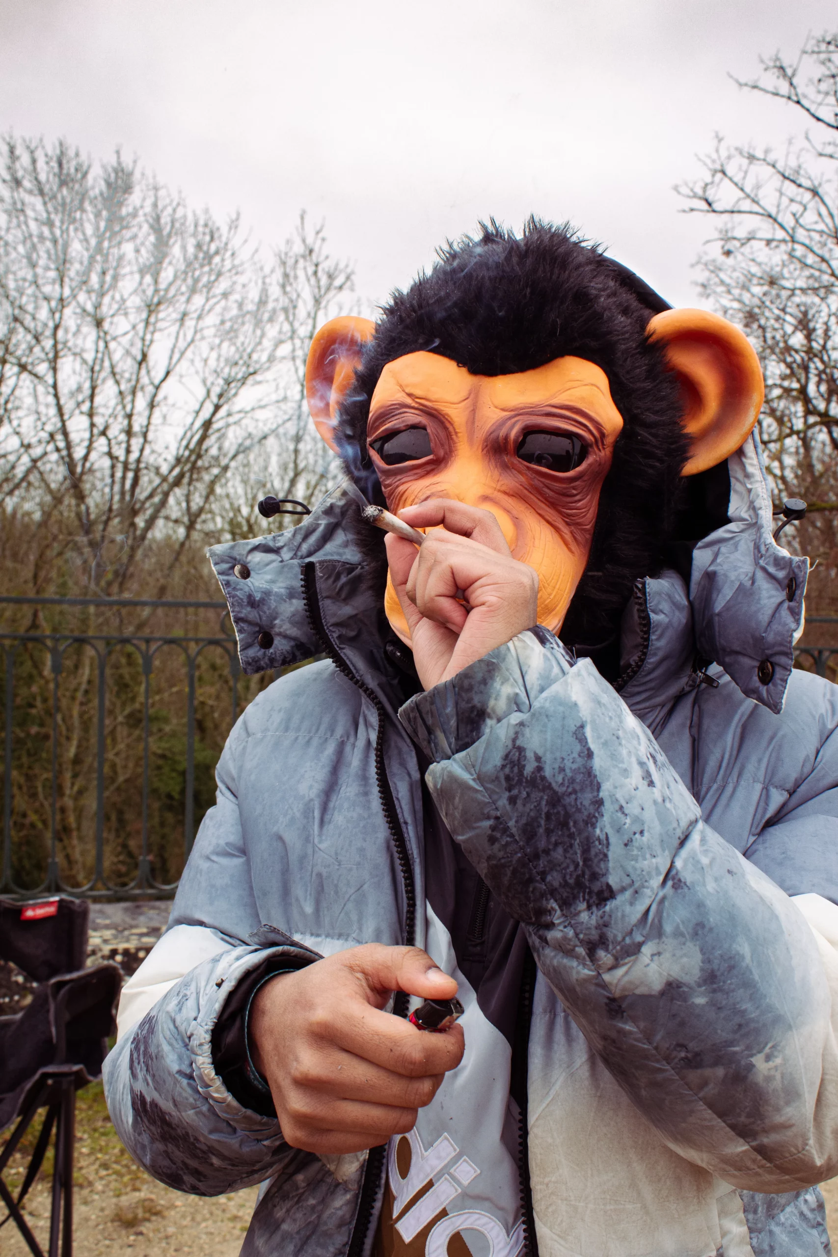 Un homme en doudoune et masque de singe allume sa cigarette, attitude décalée et mystérieuse.