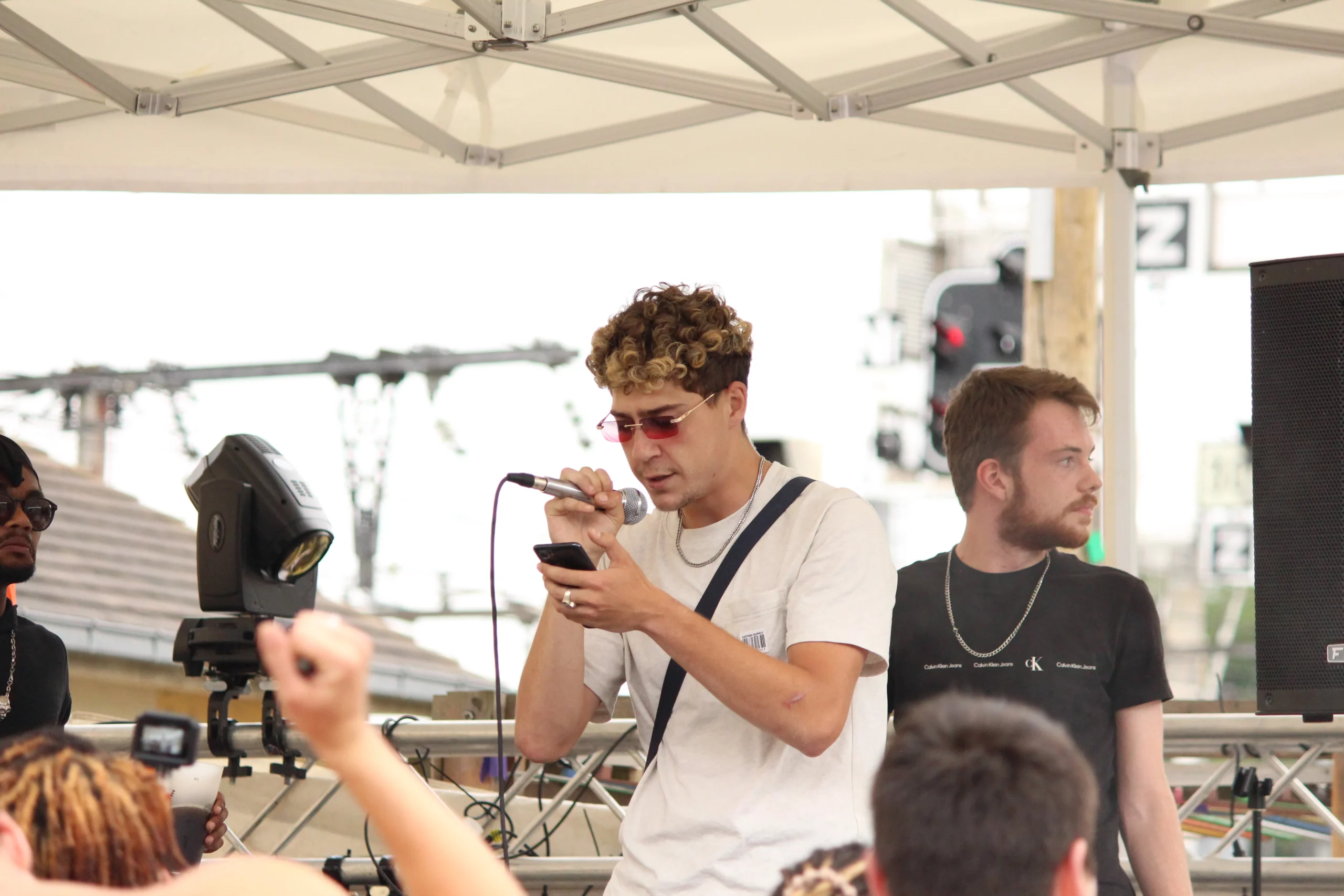 Un artiste au micro lit ses paroles sur son téléphone, concentré face au public en live.